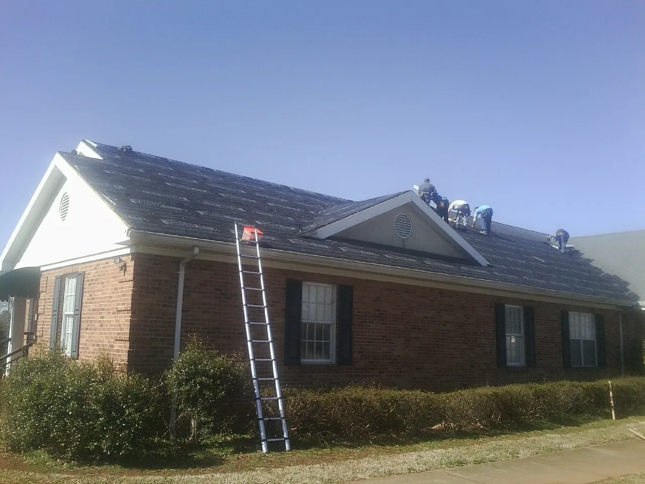 Crew tearing shingles off a brick ranch roof with a ladder set — Metal Roof Repair work by our crew in Silver Lake