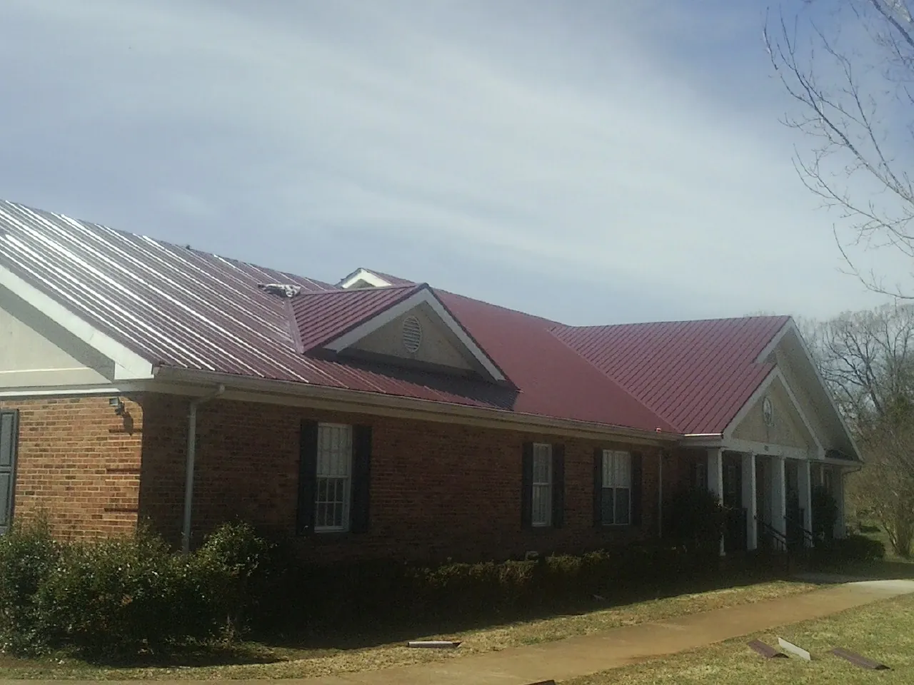Red metal roof with gabled entries on a long brick building, from a Hail Damage Roof Repair job in Silver Lake