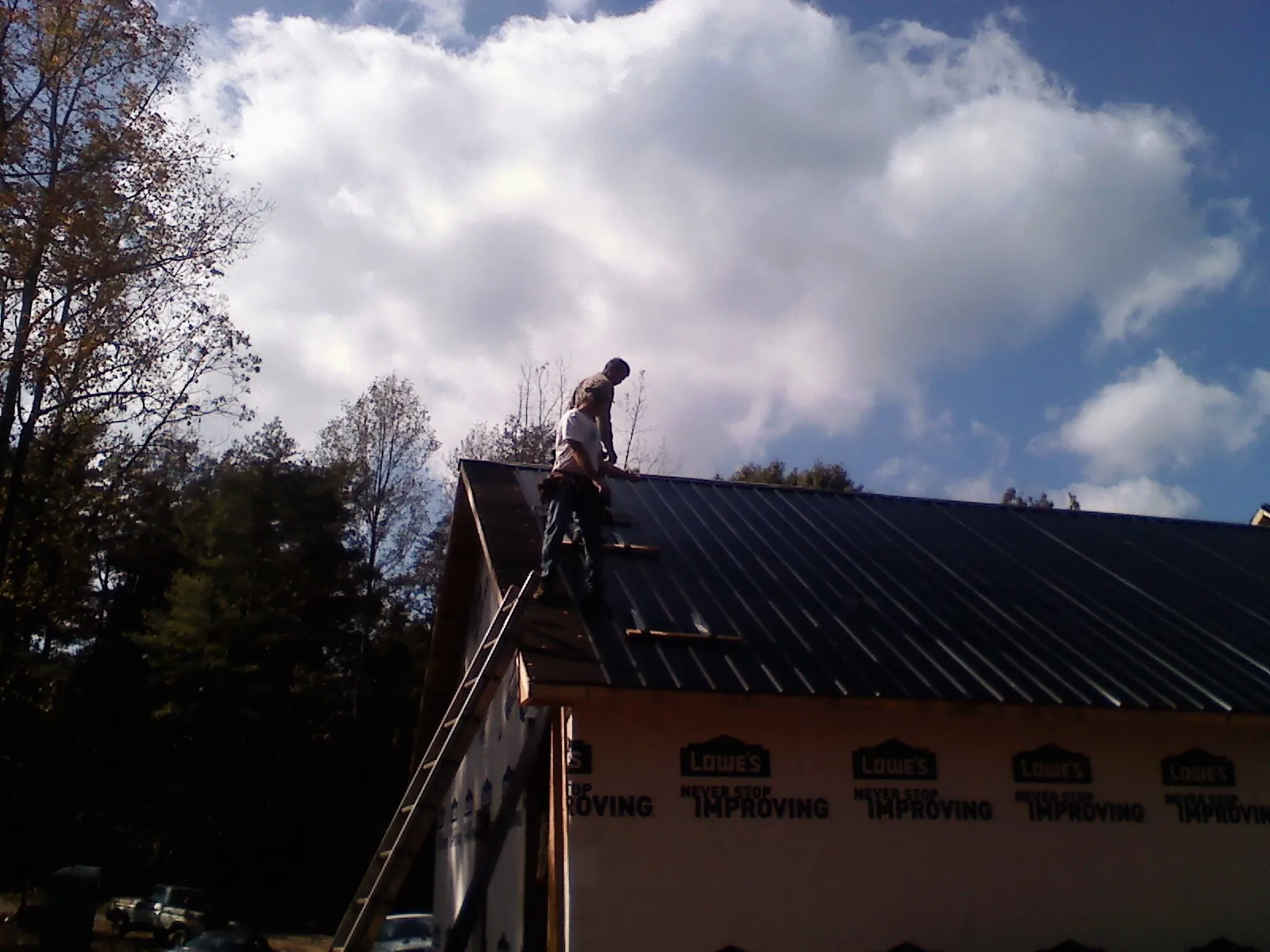 Roofer fastening dark metal panels high against a cloudy sky, from a Roof Inspection job in Silver Lake